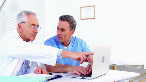 Male-doctor-and-colleague-discussing-over-laptop