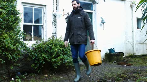 Man-walking-out-of-door-and-carrying-bucket-of-water