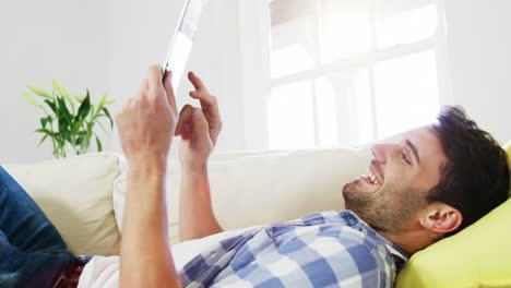 Man-using-digital-tablet-while-relaxing-on-sofa