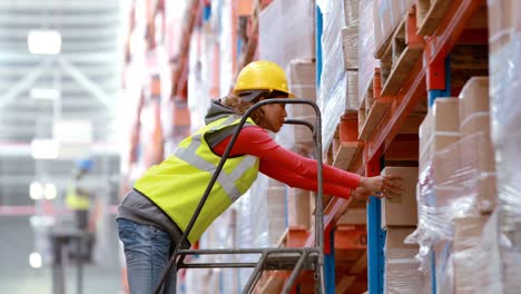 Male-warehouse-worker-using-ladder-to-arrange-cardboard-box
