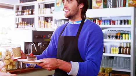 Waiter-serving-coffee-and-cupcake-to-customer-at-counter