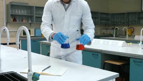 Scientist-with-sample-of-red-and-blue-chemical-writing-his-notes