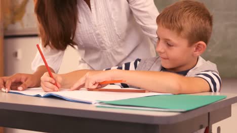 Teacher-helping-a-boy-with-his-homework-in-classroom