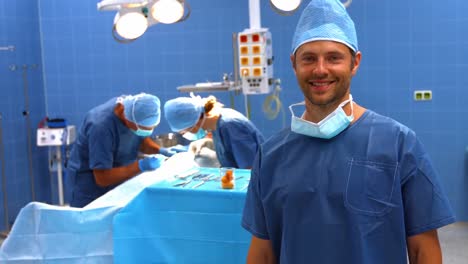 Surgeon-looking-at-camera-while-colleagues-performing-operation