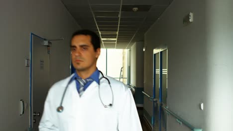 Male-doctor-holding-a-clipboard-and-walking-in-passageway-of-hospital