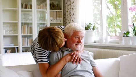 Senior-woman-embracing-man-at-home-in-living-room