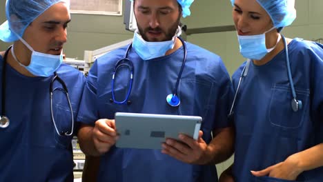 Männliche-Und-Weibliche-Chirurgen-Diskutieren-über-Ein-Digitales-Tablet-Im-Operationssaal