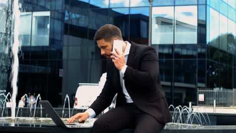 Businessman-using-laptop-while-talking-on-phone