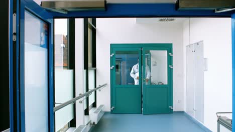 Male-doctor-holding-a-clipboard-and-walking-in-passageway-of-hospital