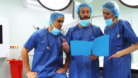 Cirujanos-Masculinos-Y-Femeninos-Discutiendo-Sobre-El-Informe-En-La-Sala-De-Operaciones