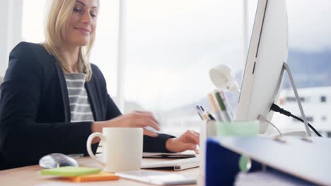 Businesswoman-drinking-cup-of-coffee-while-working-on-computer-