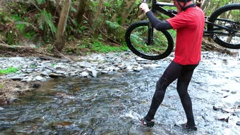 Mountain-biker-carrying-bicycle-while-crossing-creek