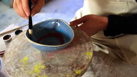 Mid-section-of-male-potter-painting-on-bowl