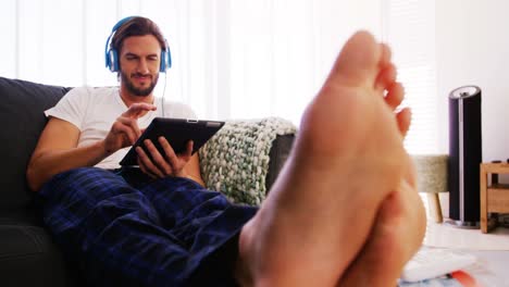 Mann-Hört-Musik-Auf-Digitalem-Tablet-Im-Wohnzimmer