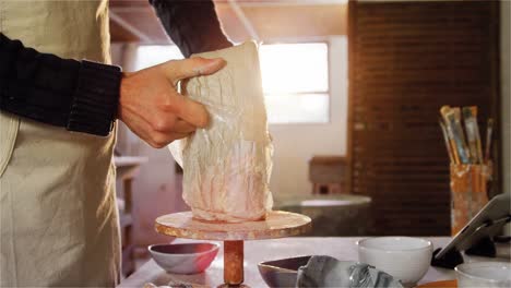 Potter-removing-plastic-cover-from-molding-clay-in-pottery-workshop