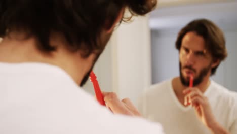Man-looking-in-mirror-while-brushing-his-teeth-in-bathroom