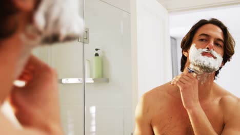 Man-reflecting-in-mirror-while-shaving-his-beared