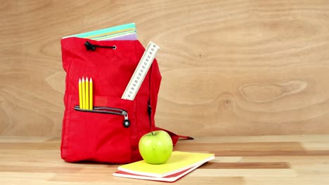 Close-up-of-school-bag-with-books,-apple-and-stationery