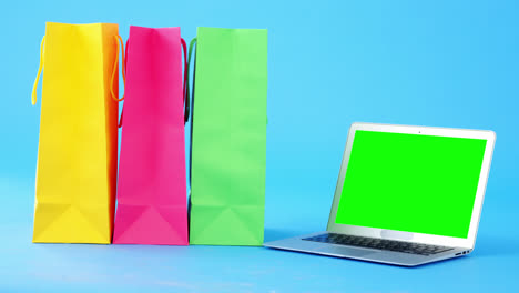 Multicolored-shopping-bags-and-laptop-on-blue-background