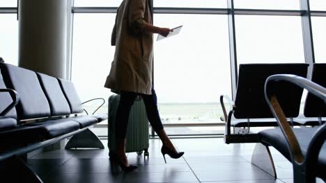 Woman-holding-digital-tablet-and-walking-with-luggage-