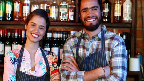 Portrait-of-barmaid-and-barman-standing-with-arms-crossed-at-bar-counter
