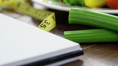 Vegetable-salad-in-plate-with-measurement-tape-and-spiral-notebook-on-table