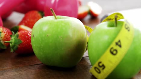 Dumbbells-and-fruits-with-measurement-tape-on-wooden-table
