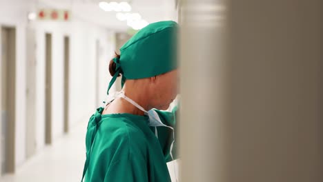 Tensed-female-surgeon-leaning-on-wall-in-corridor