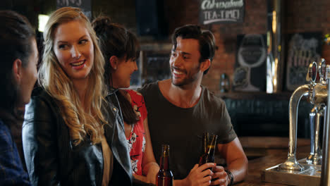 Smiling-group-of-friends-interacting-while-having-bottle-of-beer