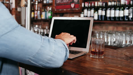 Man-using-laptop-while-having-whisky-at-counter