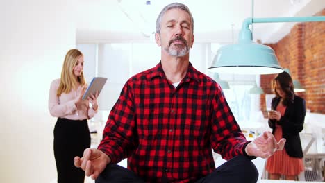 Male-executive-performing-yoga-while-his-executive-standing-in-background