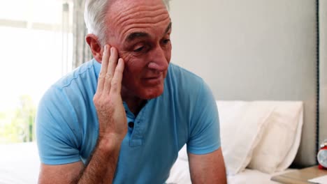 Tense-senior-man-sitting-on-bed-in-bedroom