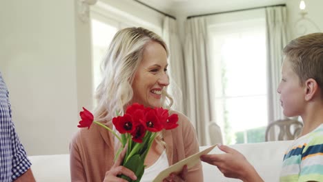 Son-offering-bunch-of-flowers-to-his-mother-in-living-room