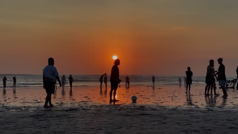 Verbrannter-Orange-goldener-Sonnenuntergang-Am-Strand,-Während-Männer-Barfuß-Fußball-Spielen
