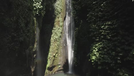 Aerial-crane-shot-ascends-lush-jungle-cliff-grotto-waterfall-in-Bali