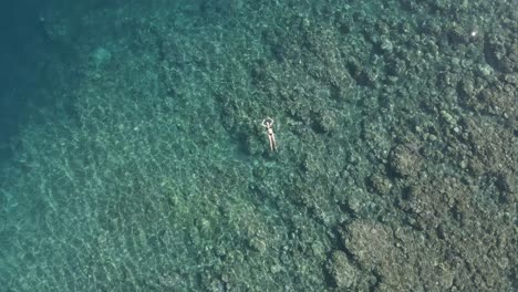 Rotating-aerial-rises-over-bikini-woman-floating-in-clear-shallow-reef