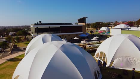 Aerial-rise-up-clip-over-people-gathering-around-white-dome-event-tents