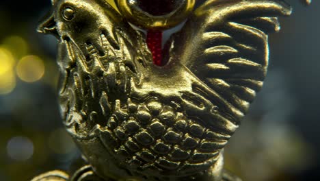 Chinese-New-Year-traditional-golden-chicken-zodiac-statue,-hanging-shiny-gold-rooster-sitting-on-money-coins-Asian-symbol,-glowing-background-with-blurry-depth-of-field,-cinematic-macro-pan-left-4K