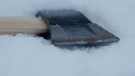 Slow-tracking-shot-along-head-of-axe-lying-in-soft-snow,-close-up