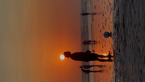 Vertical-format:-Silhouette-men-play-football-on-gold-beach-at-sunset