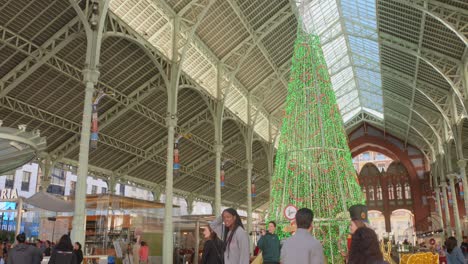 Tilt-down-shot-of-walking-around-a-street-with-the-giant-Christmas-Tree-in-the-centre-in-Valencia,-Spain-at-daytime