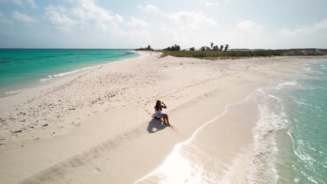 lonely-brunette-woman-in-white-enjoy-beach-jouney-sit-shore-beach,-Drone-shot-Cayo-de-Agua-Los-Roques