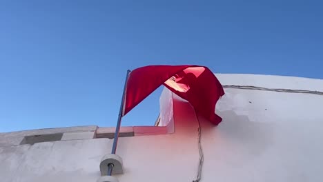 Die-Flagge-Marokkos-Windet-Sich-In-Zeitlupe,-Während-Die-Sonnenstrahlen-Sie-Auf-Der-Straße-Treffen