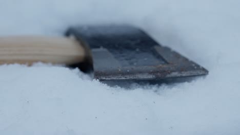 Close-up-slow-push-in-towards-axe-lying-in-powdery-snow,-macro