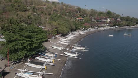 Traditional-outrigger-canoes-line-pebble-beach-on-Bali,-aerial-flyover