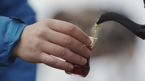 Cropped-view-of-pouring-tea-into-glass-cup-outdoors