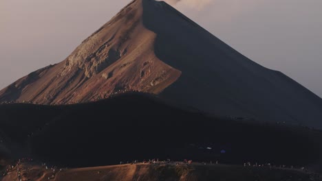 Drone-shot-tilting-away-from-hikers-in-front-of-a-smoking-Volcano-in-Guatemala