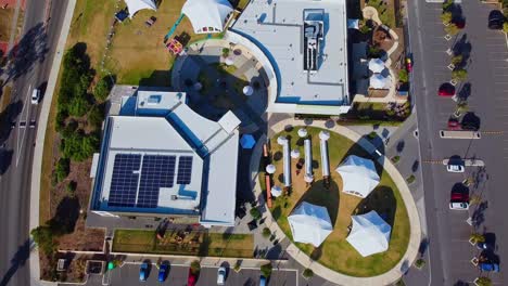 Birds-Eye-View-Over-Buildings-with-Rooftop-Solar,-White-Dome-Tents-On-Lawn-Ready-For-Event