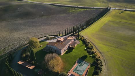 Cinematic-aerial-overview-of-mansion-villa-on-top-of-large-agricultural-farm-with-vibrant-green-land,-Val-d'Orcia-Tuscany