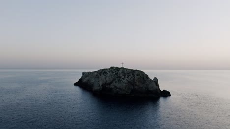 Aerial-footage-flying-towards-and-over-a-cross-on-the-small-island-of-Scoglio-dell'Eremita-in-southern-Italy